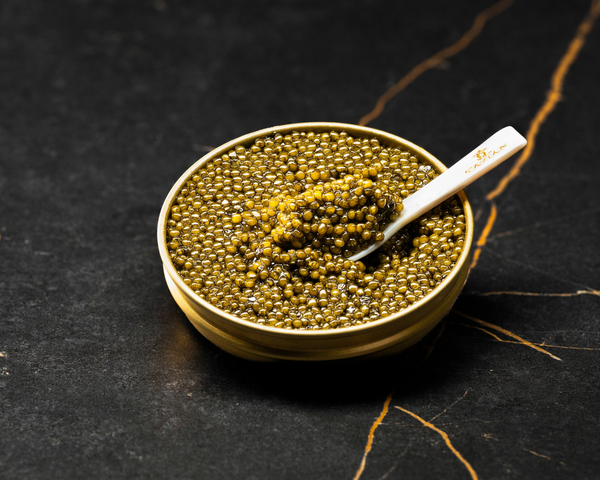 Golden caviar pearls in a gold tin with a mother-of-pearl spoon holding a serving of Cavian Royal Premimu Gold caviar.