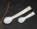 Close-up of two white mother-of-pearl caviar serving spoons in different sizes featuring engraved gold Cavian logos.