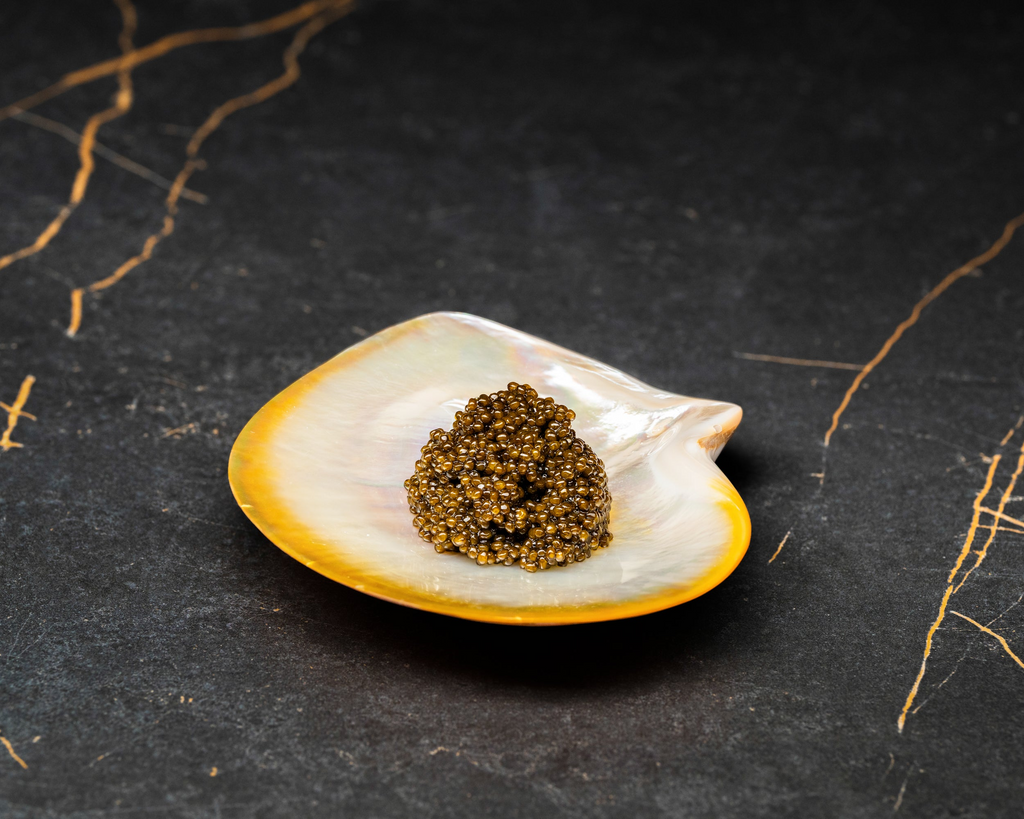 A portion of premium brown caviar pearls served on a natural iridescent mother-of-pearl shell.