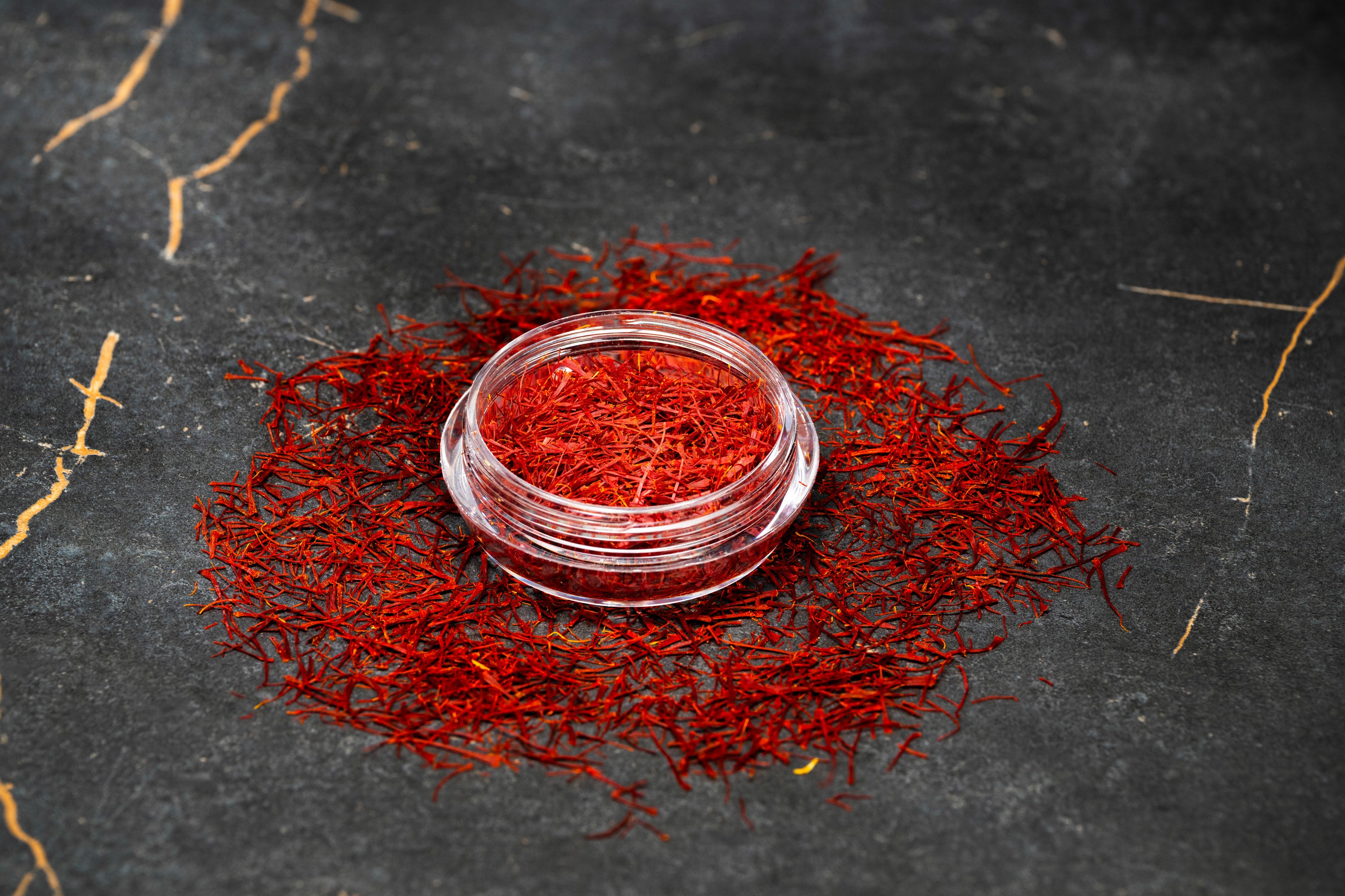 Vibrant red Persian saffron threads displayed in a clear glass jar surrounded by loose saffron strands.