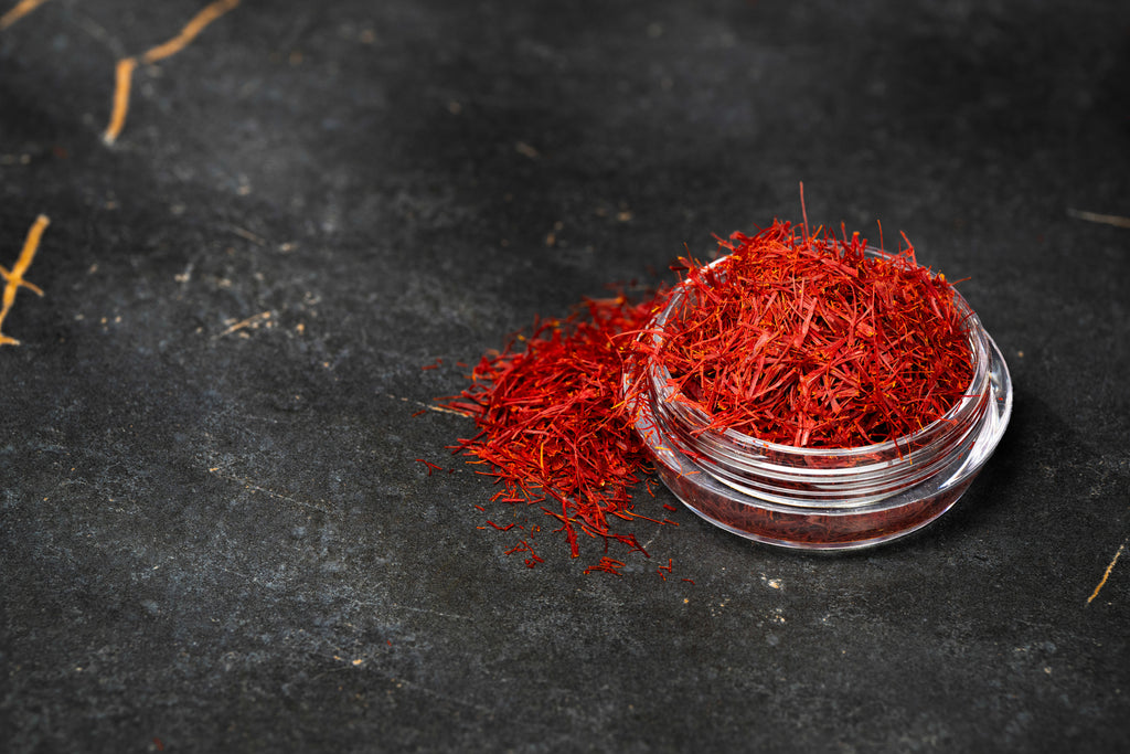 Premium red saffron threads displayed in a clear glass bowl on an elegant black marble surface.